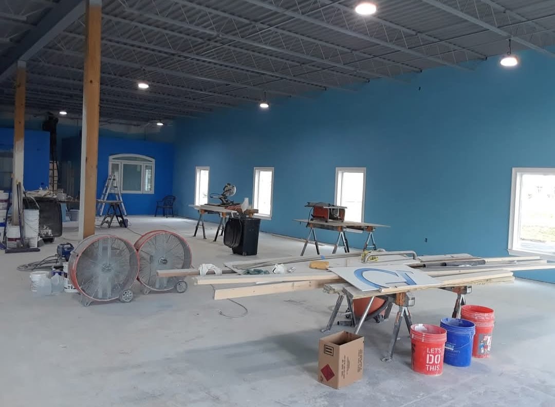 A spacious room with blue walls, featuring construction tools and materials scattered around, indicating ongoing renovation work. Natural light filters through several windows.