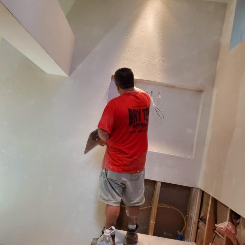 A worker is applying plaster to a wall in a partially constructed room. The focus is on the craftsmanship and the ongoing renovation process.