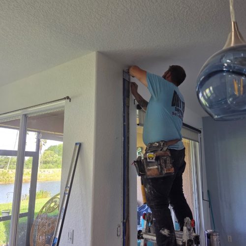 A worker is installing a fixture on the ceiling while standing on a ladder in a well-lit room. The image is labeled "BEFORE" to indicate the state prior to renovations.